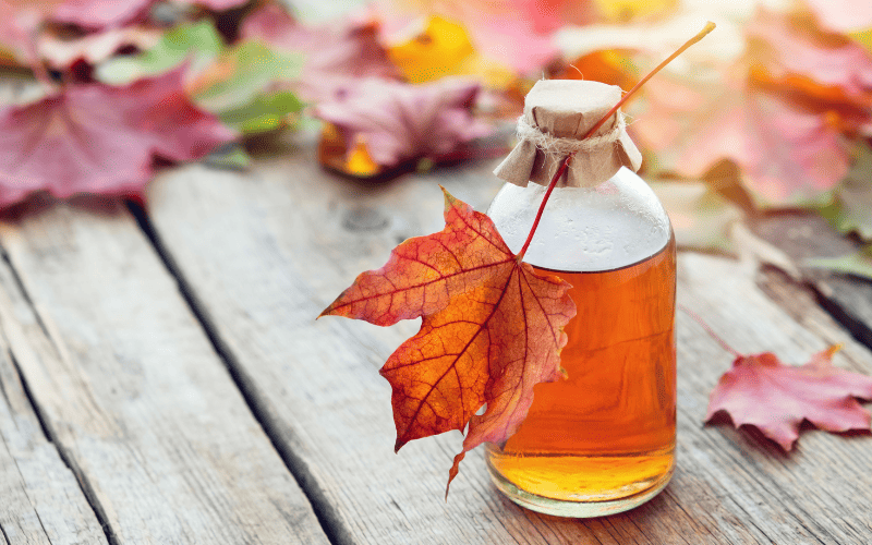 Best Substitute for Honey: 9 Alternatives to Sweeten Your Recipes Kelly Bejelly A small jar of maple syrup stands on a wooden surface, framed by vibrant fall leaves in the background; a single orange maple leaf rests delicately on the jar's lid.