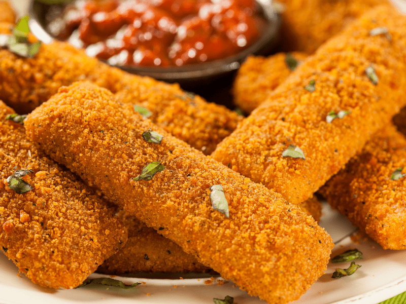 Gluten free Mozzarella Sticks close up with dip in the background 