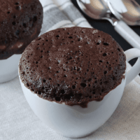 Chocolate protein mug cake on a counter with spoons in the back ground