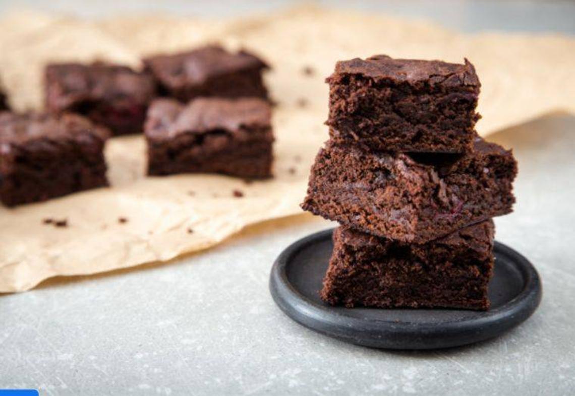 coconut flour brownies stacked on a plate with more on a parchment paper in the background