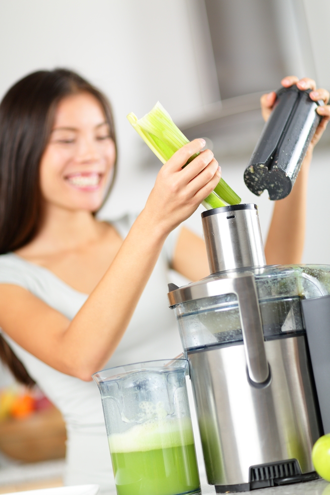Woman putting celery into a juicer to make fresh celery juice. 