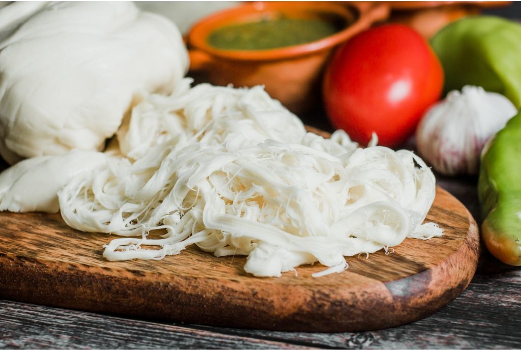 Freshly made Oaxaca cheese on a cutting board with balls of cheese. 