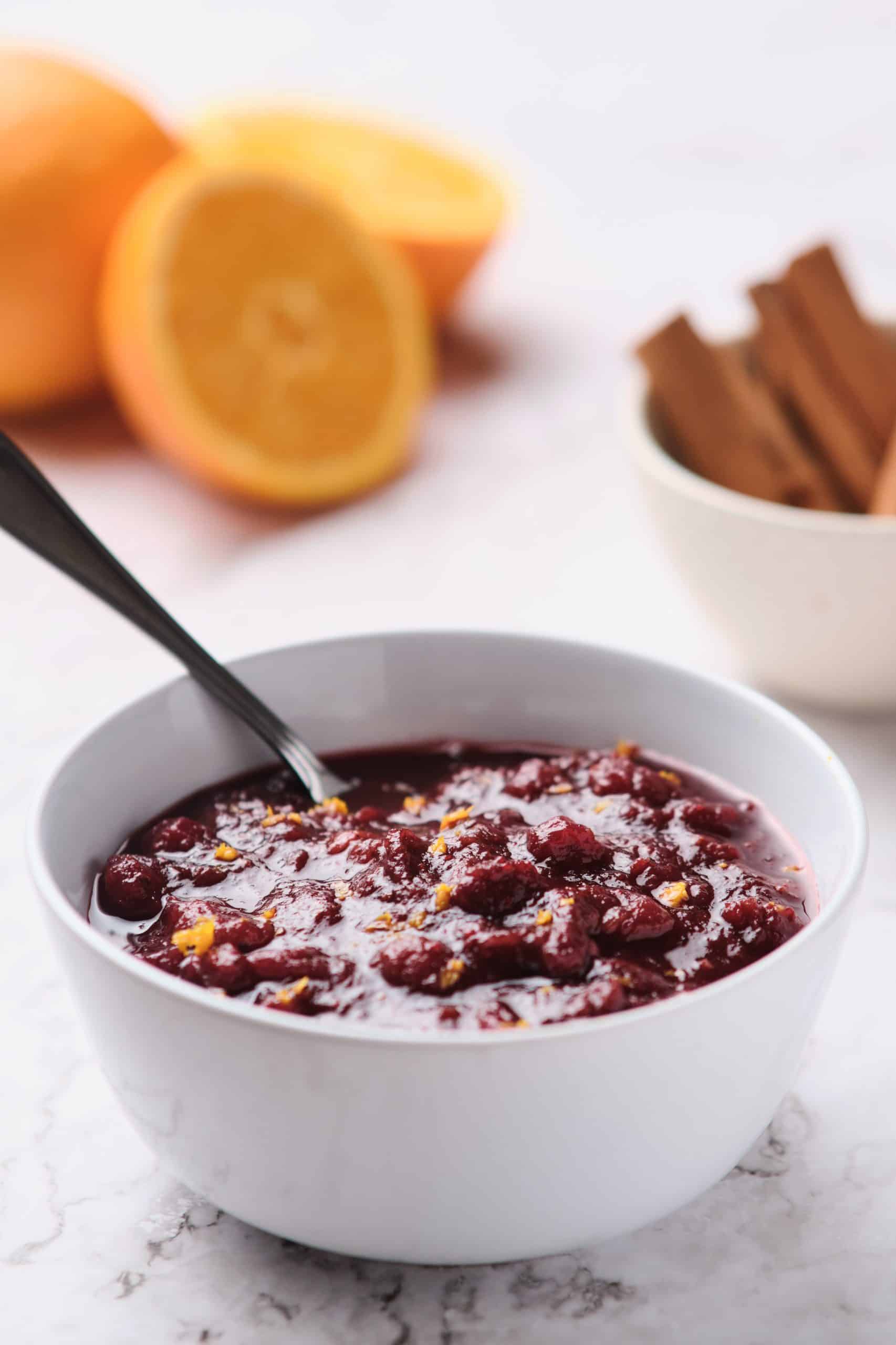 bowl of cranberry sauce on a table with spices and oranges