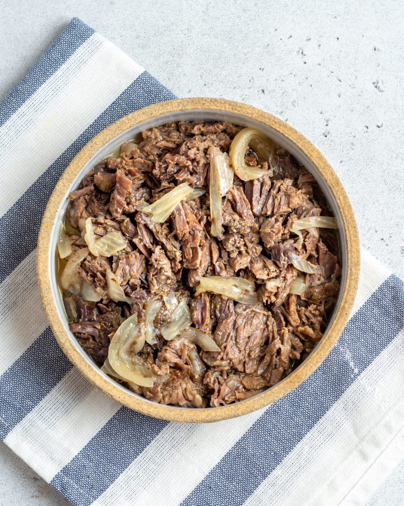 Instant pot shredded beef topped with cooked onions in a bowl 