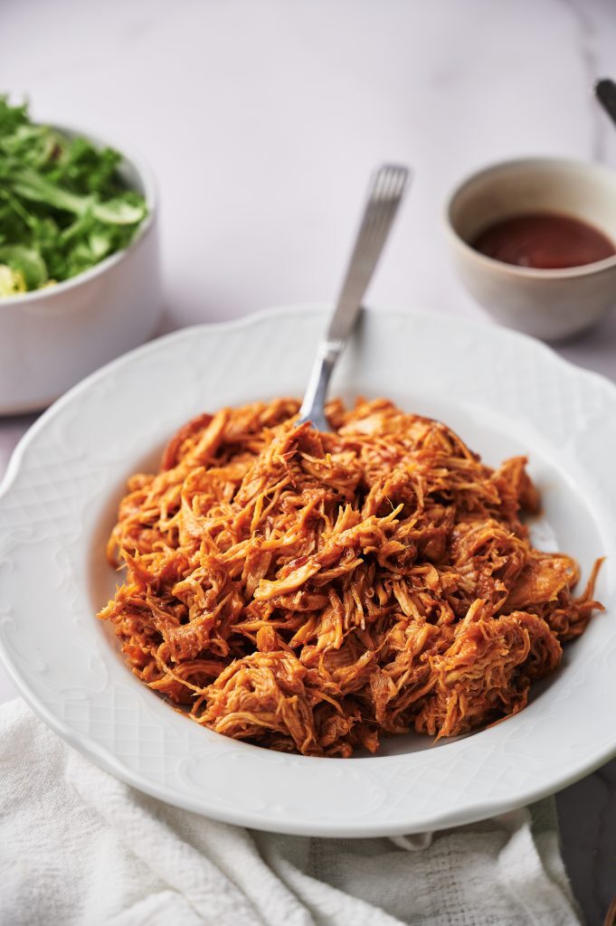 Finger Licking Crockpot bbq chicken Kelly Bejelly a bowl filled with crockpot bbq chicken with a fork sticking in it.