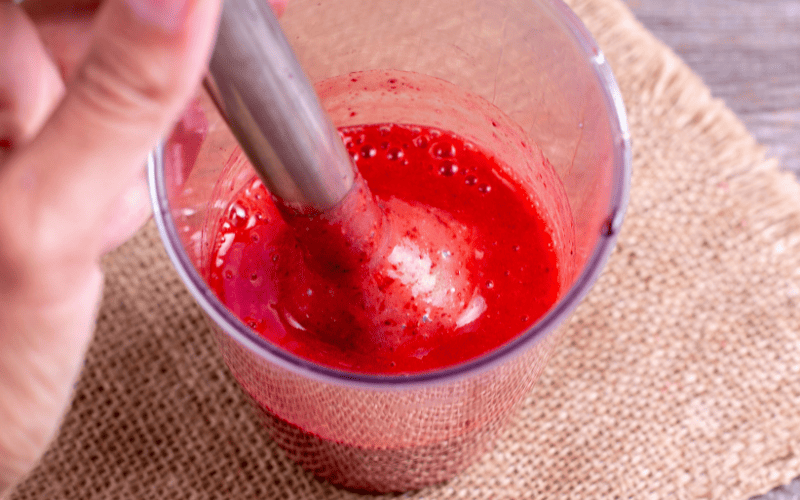 Homemade fruit roll ups: Easy Fruit leather recipe Kelly Bejelly Top-down view of a person using a stick blender to puree fresh strawberries into a vibrant and smooth mixture.